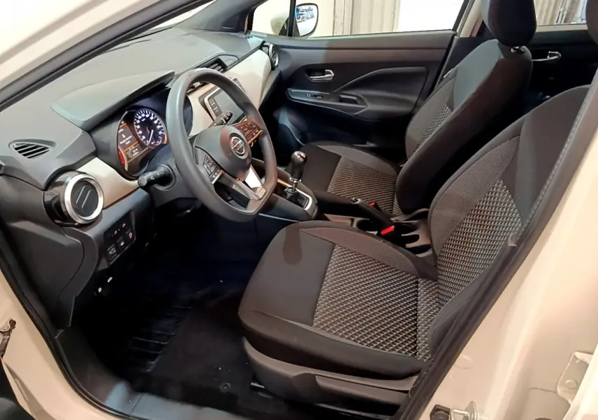 Intérieur avant côté conducteur d'une Nissan Micra blanche 2022 avec sièges tissu noirs et volant multifonctions.