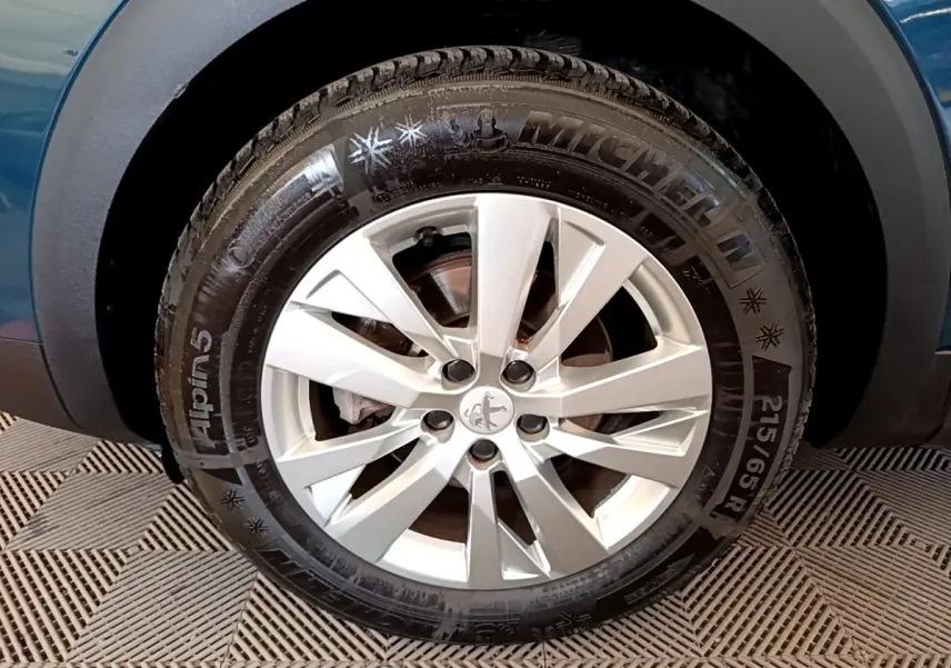 Gros plan sur la roue avant gauche d’un Peugeot 3008 bleu, mettant en valeur la jante argentée et le pneu Michelin Alpine 5.