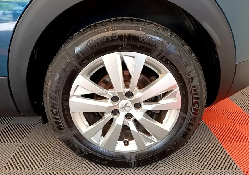 Gros plan sur la roue avant droite d’un Peugeot 3008 bleu, jante alliage argentée avec logo lion au centre.