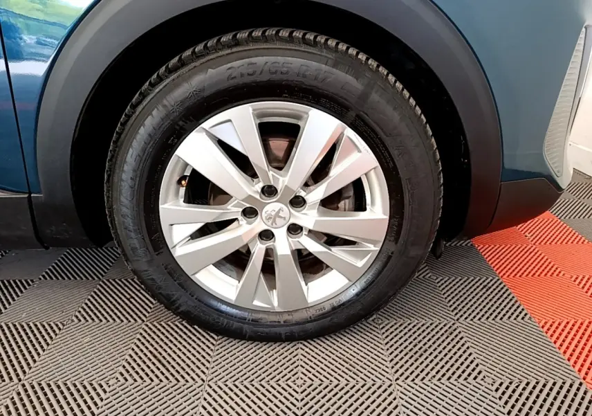 Gros plan sur la roue avant gauche d’un Peugeot 3008 bleu 2022 avec jante alliage argentée et logo lion central.
