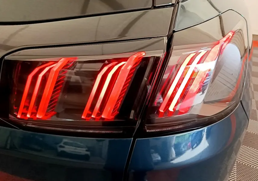 Gros plan sur le feu arrière droit rouge d’un Peugeot 3008 bleu, soulignant la carrosserie brillante et les lignes modernes.