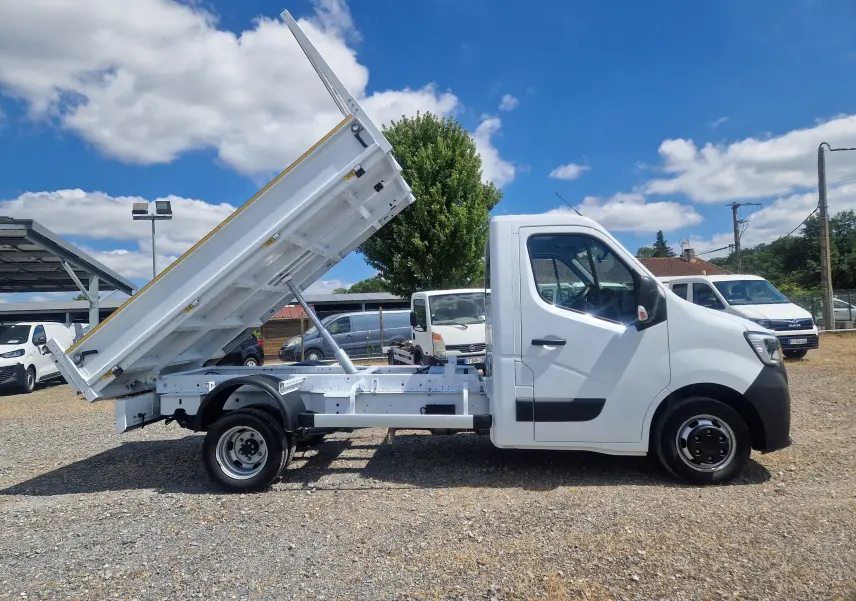 Vue latérale droite d'un Renault Master blanc 2024 avec benne basculante relevée et roues jumelées visibles.