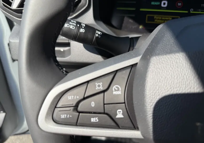 Gros plan sur les commandes au volant gauche du Dacia Duster Hybrid 155 Journey blanc glacier, avec boutons de régulateur de vitesse.