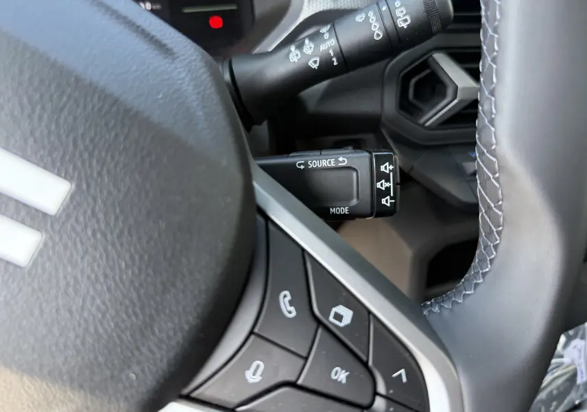 Gros plan sur la commande multimédia et le commodo d’essuie-glace côté gauche du volant du Dacia Duster Hybrid 155 blanc glacier.