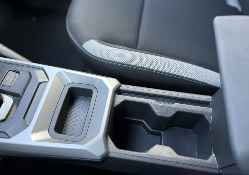 Gros plan sur la console centrale noire du Dacia Duster Hybrid 155 Journey 2026, avec porte-gobelets et accoudoir tissu gris et noir.