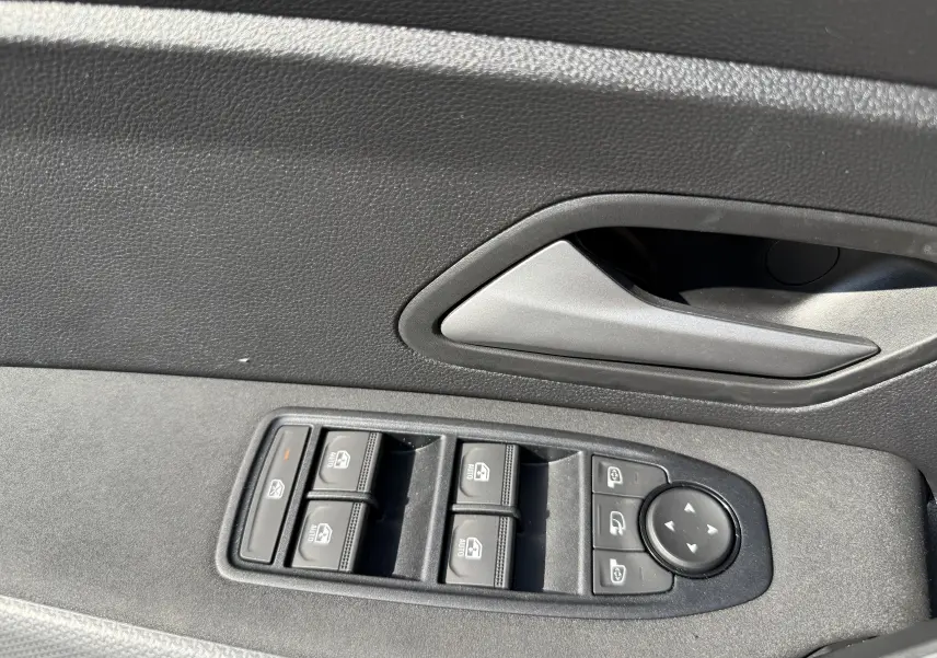 Gros plan sur la commande des vitres et rétroviseurs côté conducteur du Dacia Duster Hybrid 155 blanc glacier, intérieur noir.