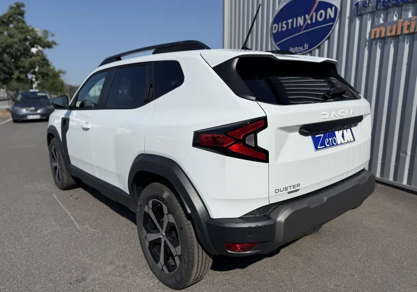 Vue 3/4 arrière droite du Dacia Duster Hybrid 155 Journey blanc glacier avec jantes noires et détails noirs contrastants.