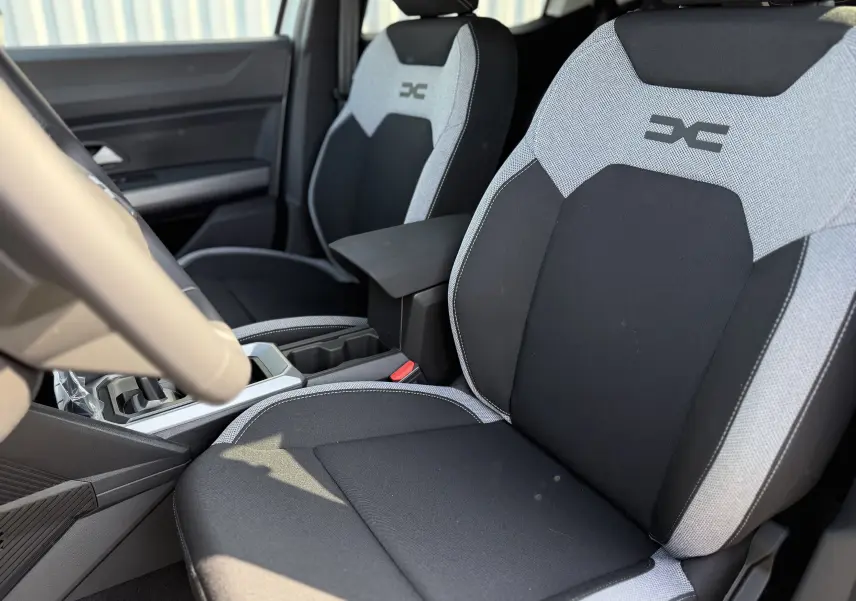 Vue intérieure rapprochée des sièges avant gris clair et noir du Dacia Duster Hybrid 155 Journey avec logo distinctif brodé.