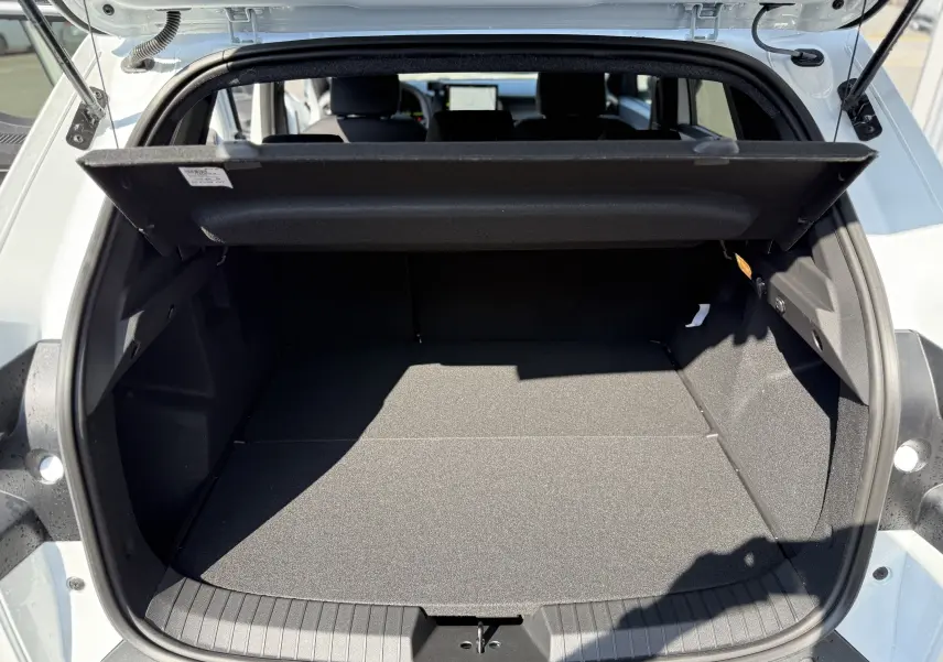 Coffre ouvert vu de l'arrière d'un Dacia Duster Hybrid 155 Journey blanc glacier, montrant un espace de chargement vide.