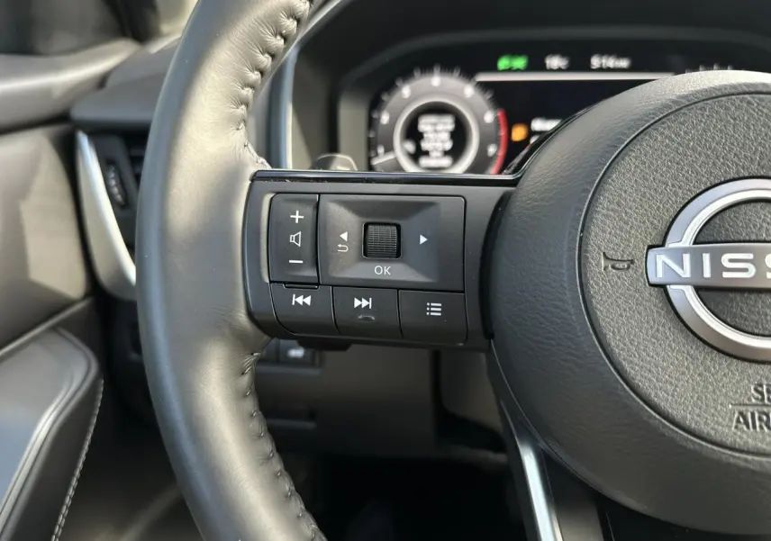 Gros plan sur le volant cuir noir du Nissan Qashqai 2025 avec commandes intégrées et tableau de bord numérique flou.