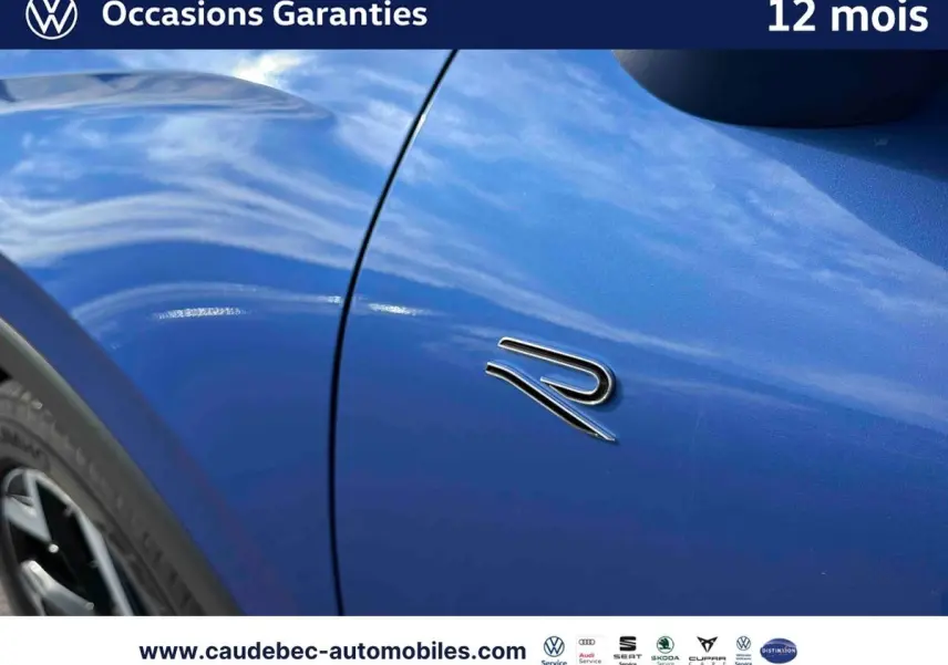 Gros plan sur l'aile avant gauche bleu métallisé du Volkswagen T-Roc avec logo R distinctif.