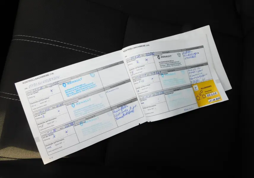 Carnet d'entretien Renault posé sur un siège noir avec surpiqûres blanches, vue rapprochée intérieure.