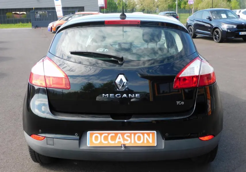 Vue arrière d'une Renault Mégane noire de 2015 avec logo et plaque "OCCASION" visible sur un parking.