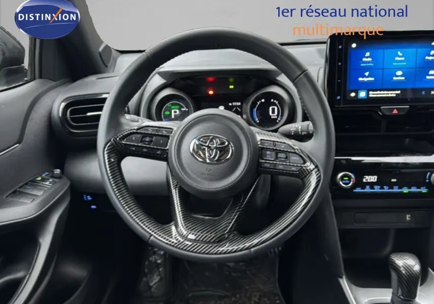 Vue intérieure du tableau de bord et volant en carbone d'une Toyota Yaris Cross 116h Design 2023 noire avec écran tactile et commandes intégrées.