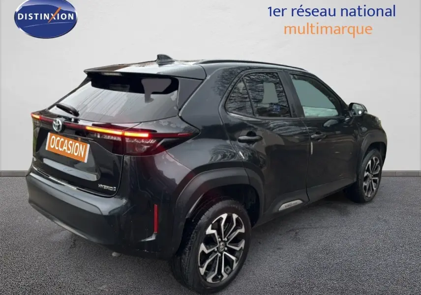 Vue 3/4 arrière droite d'une Toyota Yaris Cross 116h Design noire avec jantes bi-ton et feux arrière allumés.