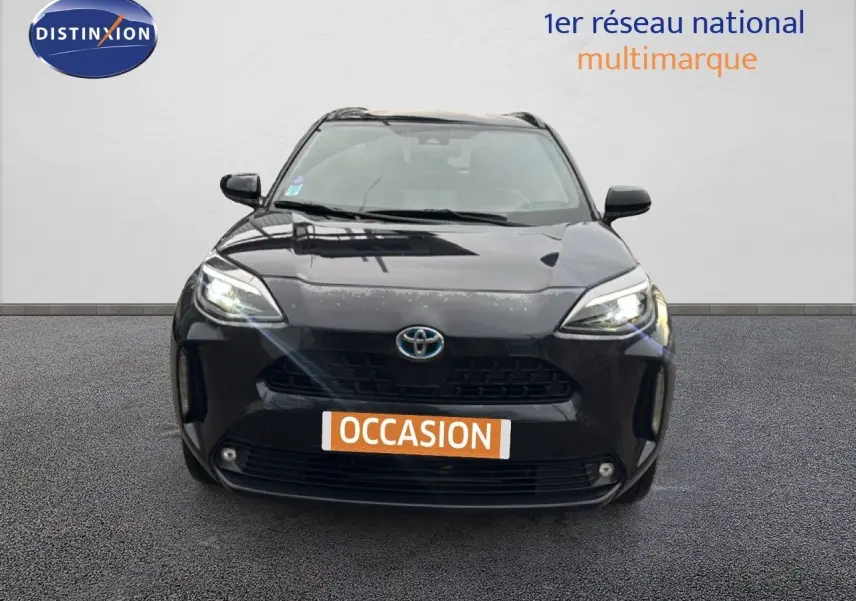 Vue frontale d'une Toyota Yaris Cross 116h Design noire de 2023 avec phares allumés sur fond neutre.