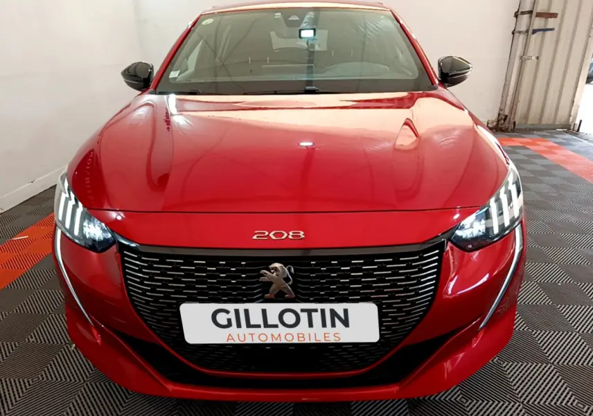 Vue frontale d'une Peugeot 208 BlueHDi 100 S&S GT Line rouge avec phares LED allumés et calandre noire distinctive.