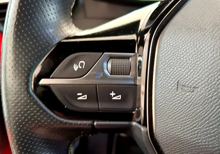Gros plan sur les commandes vocales et volume du volant en cuir perforé de la Peugeot 208 GT Line rouge.