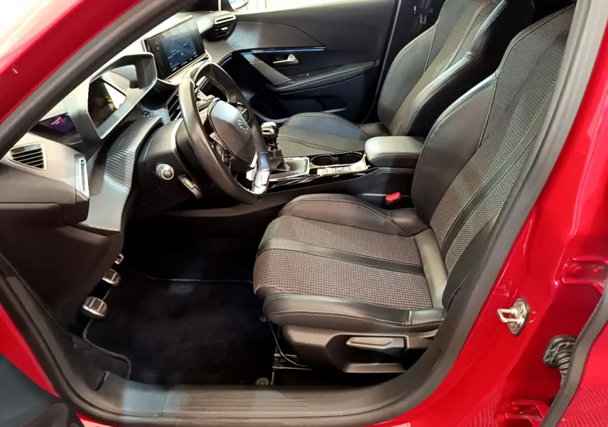 Intérieur côté conducteur de la Peugeot 208 rouge, montrant sièges sport et tableau de bord moderne avec écran tactile.