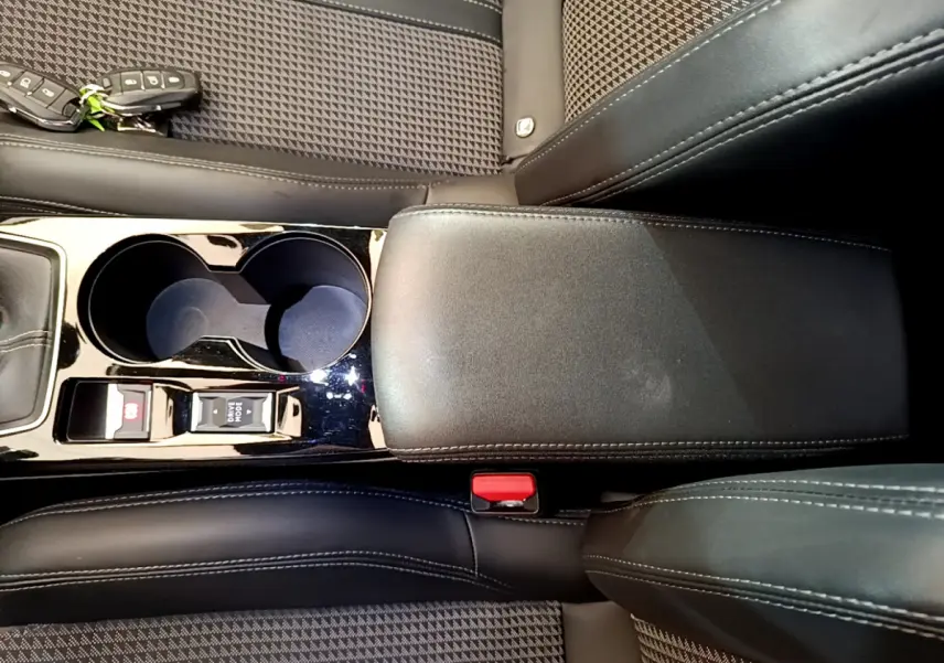 Vue rapprochée de l'accoudoir central noir et des sièges en tissu gris à motifs de la Peugeot 208 GT Line rouge.