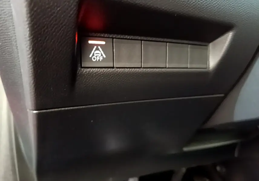 Gros plan sur le bouton d'arrêt de l'assistance au maintien de voie dans l'habitacle noir de la Peugeot 208 GT Line rouge.