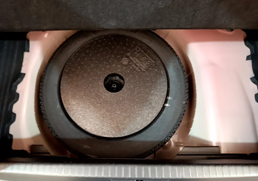 Roue galette de secours noire dans le coffre blanc d'une Peugeot 208 GT Line rouge, vue en plongée.