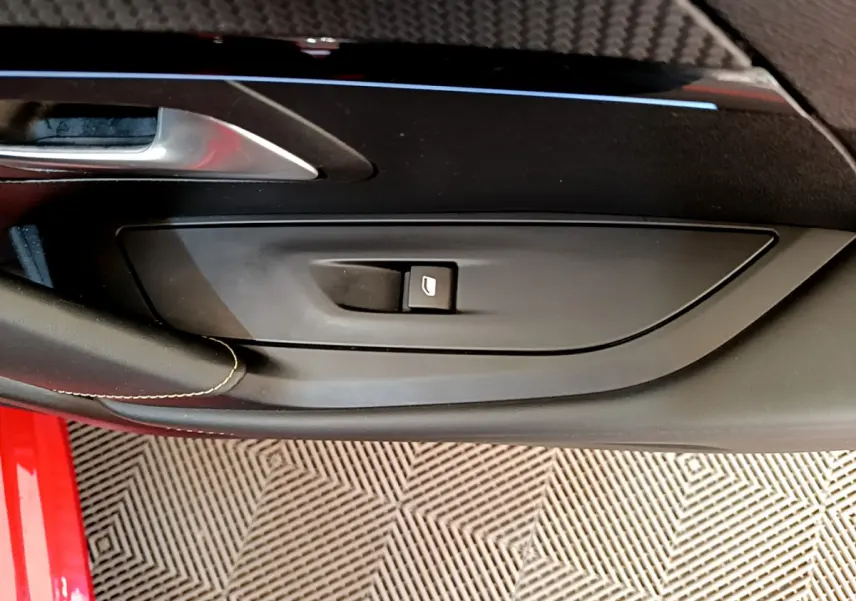 Détail de la commande de lève-vitre côté conducteur sur la porte intérieure noire d'une Peugeot 208 rouge 2020.