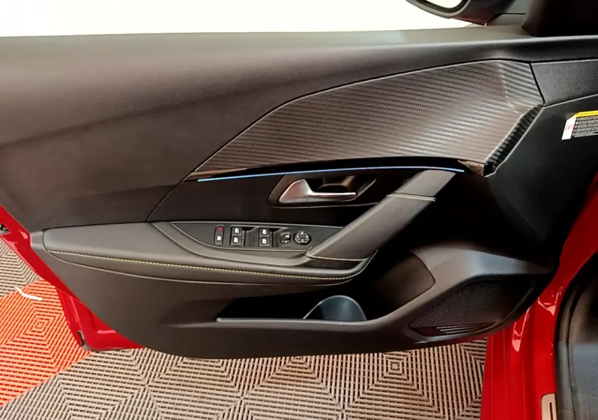 Vue rapprochée de la porte avant gauche rouge d'une Peugeot 208 GT Line avec garniture noire et surpiqûres jaunes.