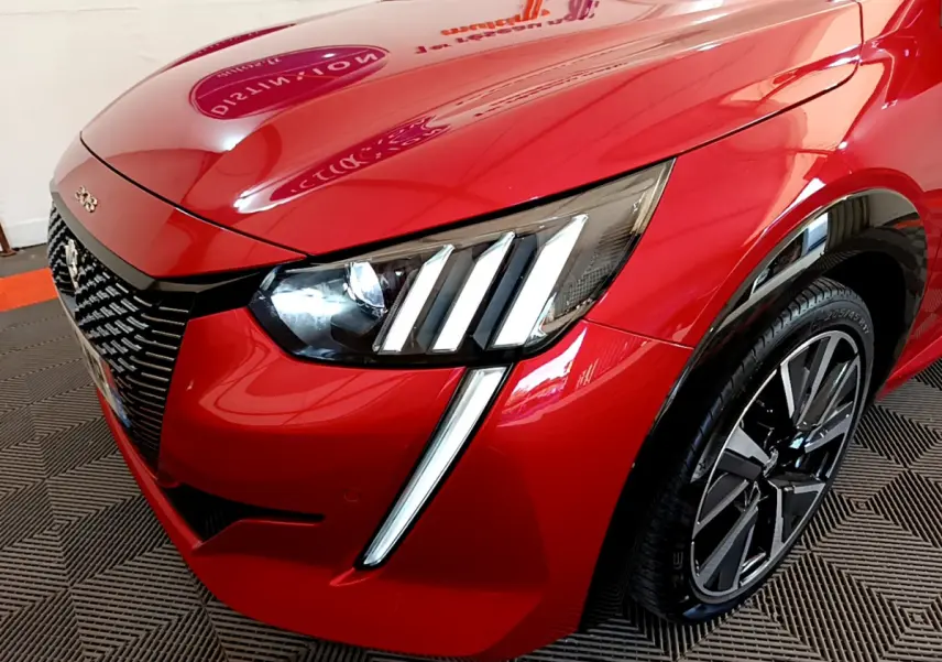 Vue 3/4 avant droit du Peugeot 208 rouge avec ses phares LED distinctifs en forme de griffes et jante alliage moderne.