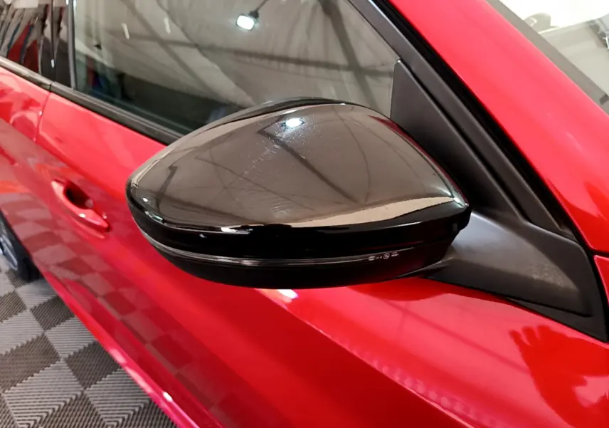 Rétroviseur noir brillant côté gauche d'une Peugeot 208 rouge vue de près sur porte avant.