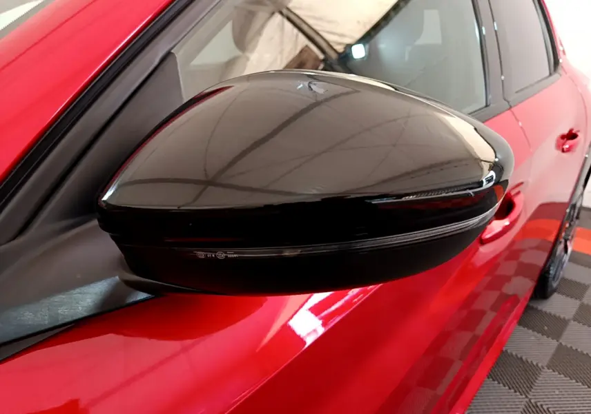 Rétroviseur noir brillant côté gauche d'une Peugeot 208 GT Line rouge vue en gros plan depuis l'avant