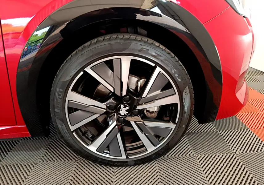Gros plan sur la roue avant droite du Peugeot 208 rouge 2020 avec jante alliage bicolore et logo lion central.