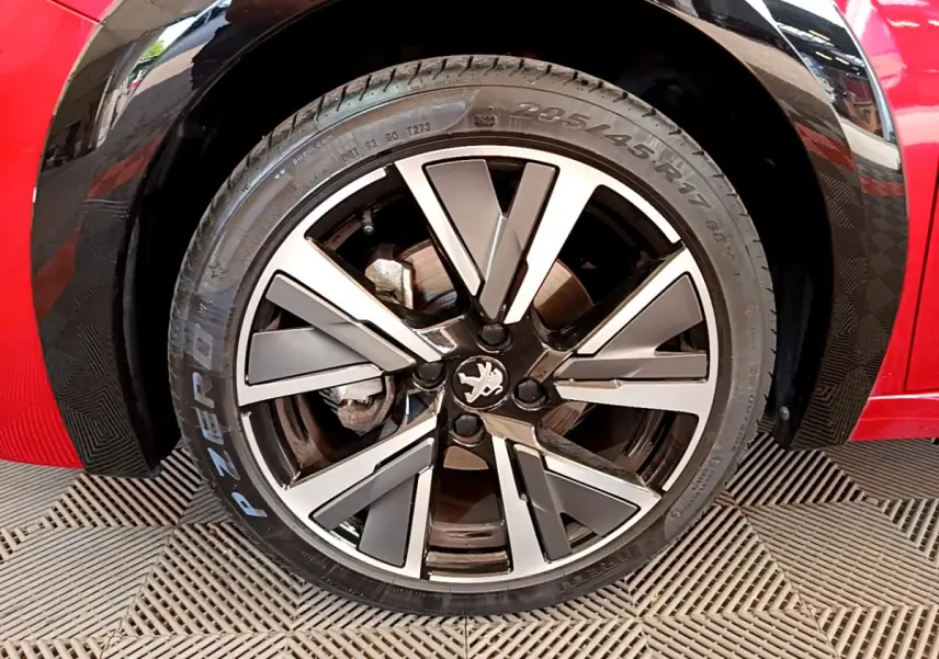 Gros plan sur la roue avant droite de la Peugeot 208 rouge avec jante alliage à design moderne et logo lion central.