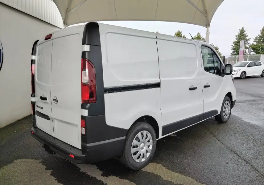 Vue 3/4 arrière droite d'un utilitaire Nissan Primastar blanc avec attelage et protections noires sur pare-chocs et bas de caisse.