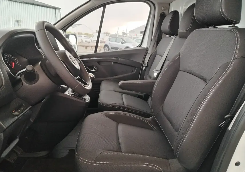 Vue intérieure côté conducteur du Nissan Primastar 2025 blanc, sièges noirs avec coutures blanches et volant multifonction.