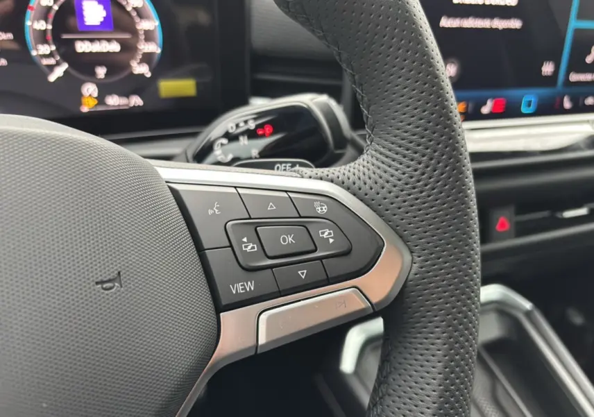 Gros plan sur le volant cuir perforé du Volkswagen T-Roc 2026 avec commandes multifonctions et affichage digital en arrière-plan.