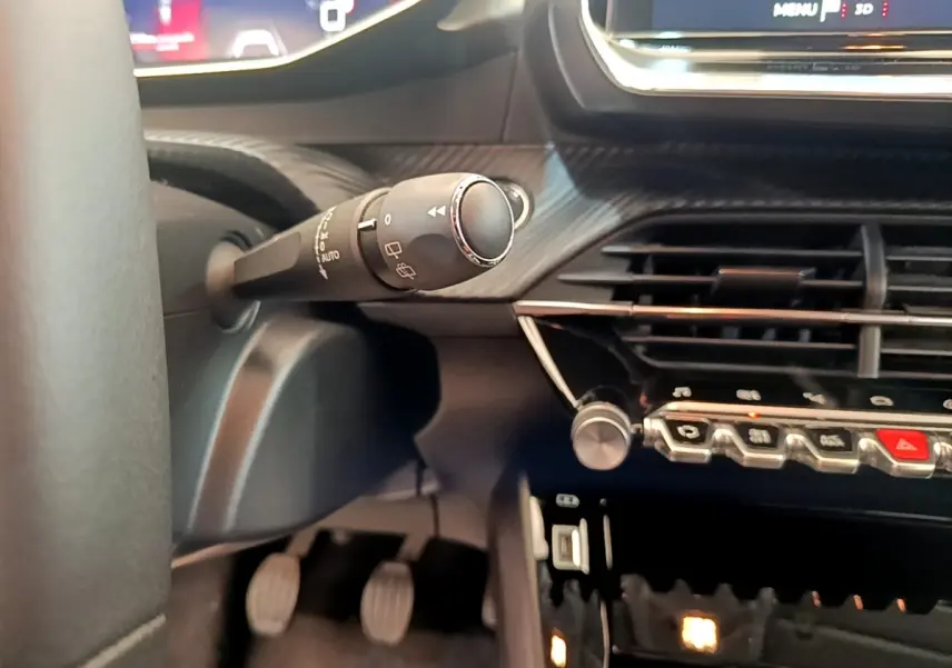 Gros plan sur la commande d’essuie-glace et la console centrale noire du tableau de bord de la Peugeot 208 PureTech 100.