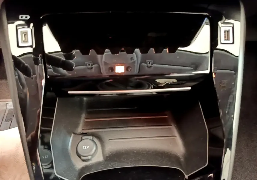 Gros plan sur la console centrale noire du Peugeot 208 PureTech 100, avec prise 12V visible au centre.
