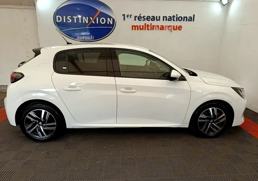 Profil droit d'une Peugeot 208 blanche de 2021, avec jantes alliage noires et vitres teintées, en intérieur showroom.