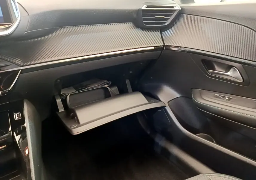 Vue intérieure côté passager du tableau de bord noir et boîte à gants ouverte de la Peugeot 208 PureTech 100 blanche.