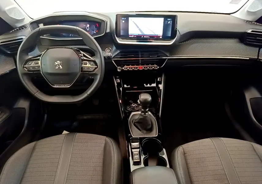 Vue intérieure frontale de la Peugeot 208 blanche, volant cuir, écran tactile 10 pouces et levier de vitesse manuel.