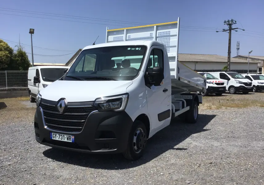 Vue 3/4 avant droite d’un Renault Master Benne blanc avec benne relevée et roues jumelées sur un parking.