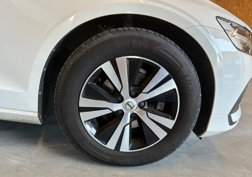 Gros plan sur la roue avant droite d’une Volvo V60 blanche de 2020, jante alliage bicolore et pneu Vredestein.