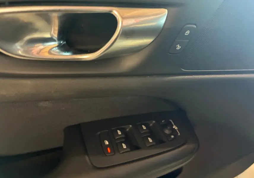 Gros plan sur la poignée intérieure et les commandes des vitres côté conducteur d’un Volvo V60 D3 blanc, intérieur noir.