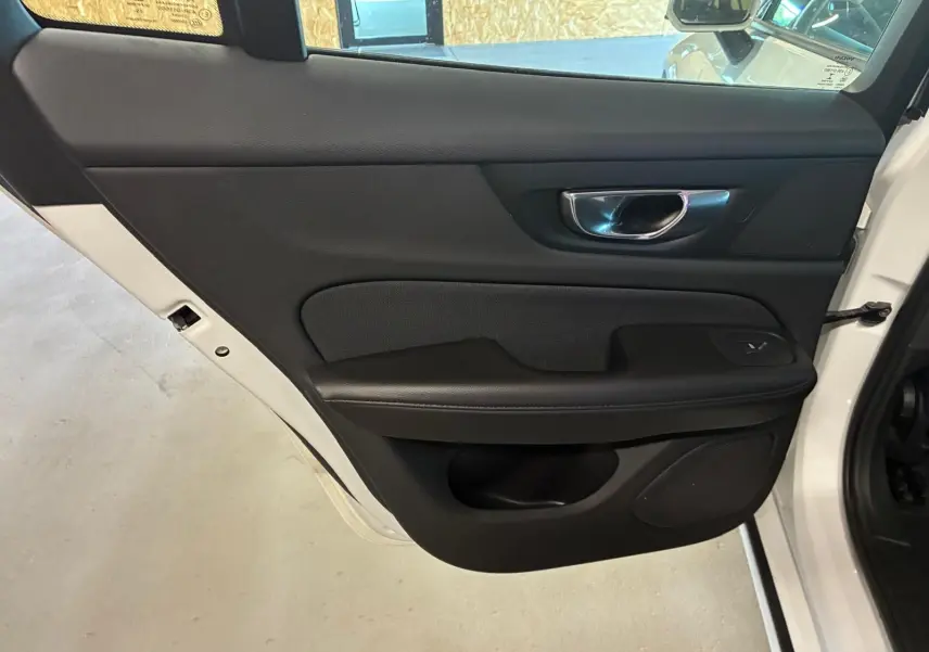 Vue rapprochée de la porte arrière gauche noire intérieure du Volvo V60 blanc, avec poignée chromée et bouton de vitre.