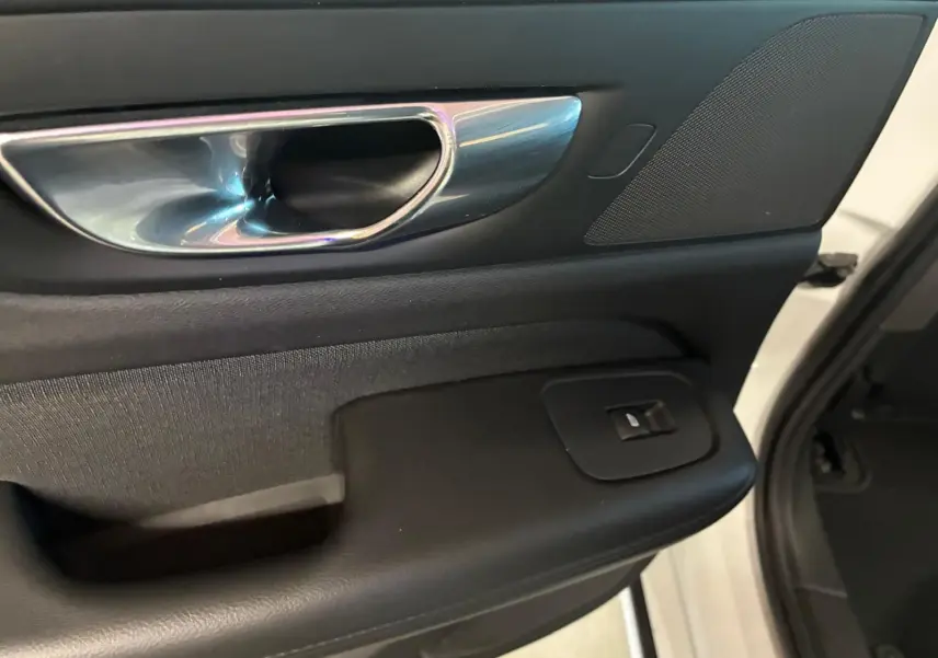 Poignée intérieure côté gauche de la porte avant d'une Volvo V60 blanche, avec bouton de commande de vitre et finition noire.