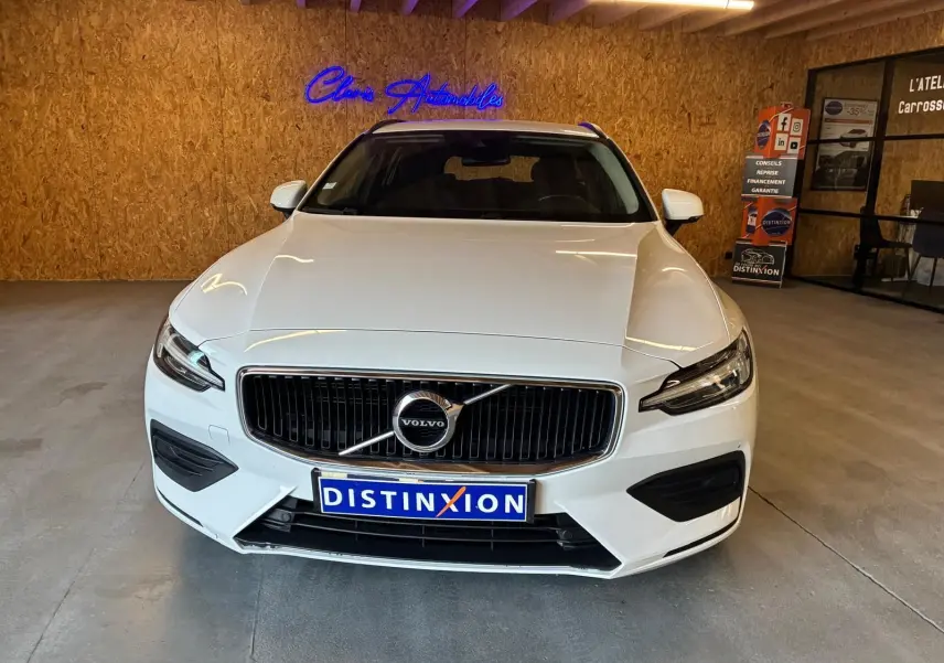 Vue avant d'un Volvo V60 D3 blanc 2020 avec calandre noire et logo centré dans un showroom.