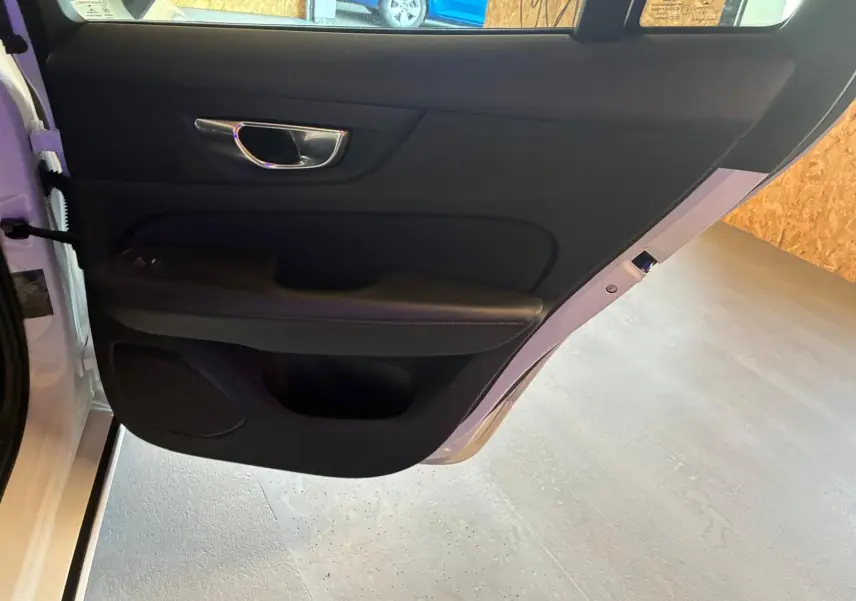 Vue intérieure de la porte arrière gauche noire d'une Volvo V60 D3 blanche, avec poignée chromée et haut-parleur intégré.