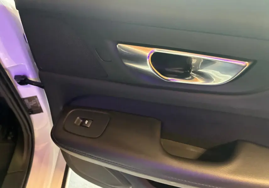 Gros plan sur la poignée intérieure côté gauche de la porte avant d’une Volvo V60 blanche avec bouton de commande de vitre.