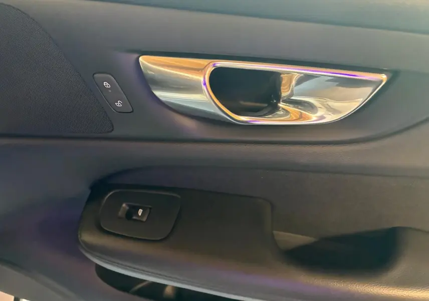 Poignée intérieure chromée et commandes de verrouillage sur la porte côté gauche d’un Volvo V60 blanc, vue rapprochée.